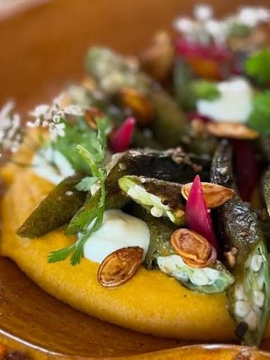 Prato autoral com legumes, sementes de abóbora e flores sobre purê de abóbora